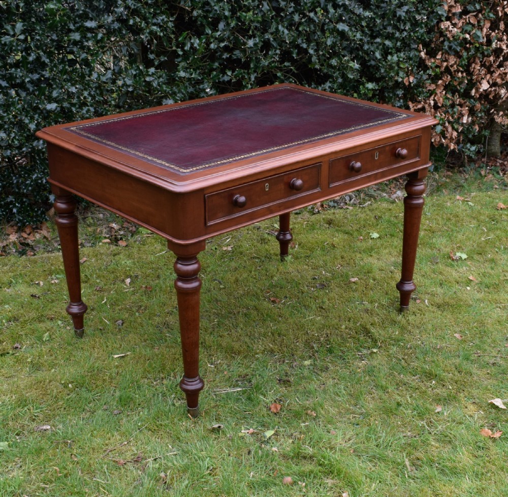 A Victorian mahogany writing table featuring a dark red leather insert top, two frieze drawers with wooden knobs, and four turned legs. View II