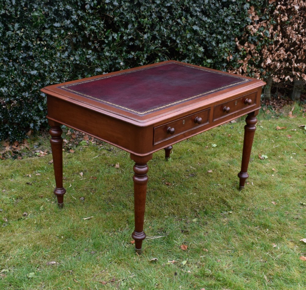 A Victorian mahogany writing table featuring a dark red leather insert top, two frieze drawers with wooden knobs, and four turned legs. View III