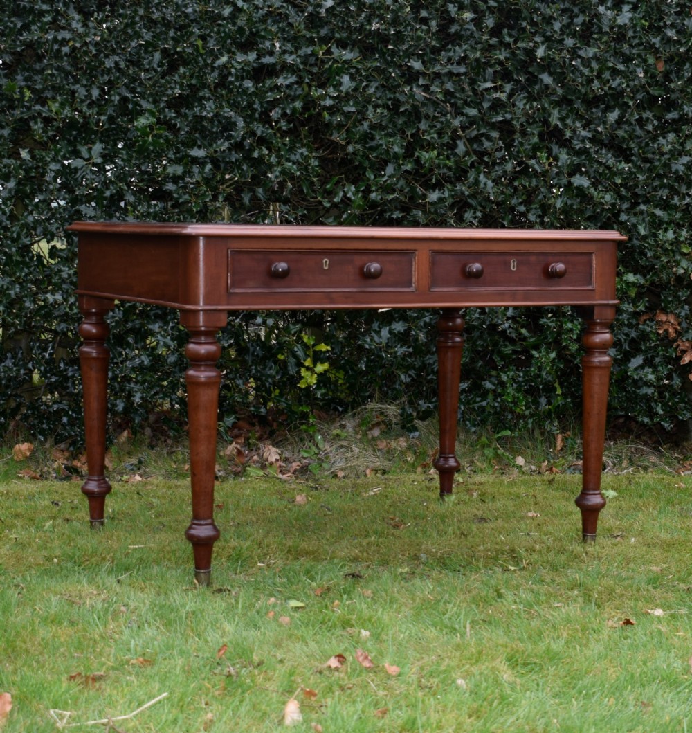 A Victorian mahogany writing table featuring a dark red leather insert top, two frieze drawers with wooden knobs, and four turned legs. View V