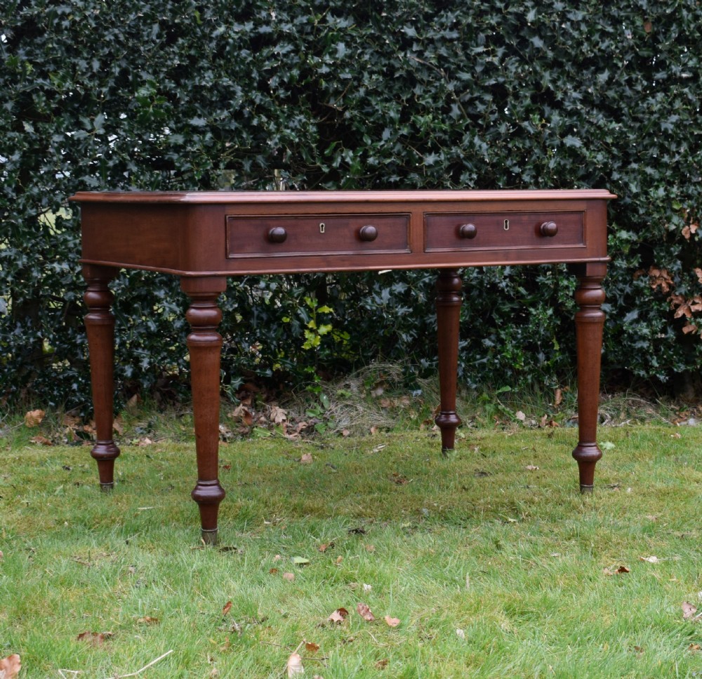 A Victorian mahogany writing table featuring a dark red leather insert top, two frieze drawers with wooden knobs, and four turned legs. View VI