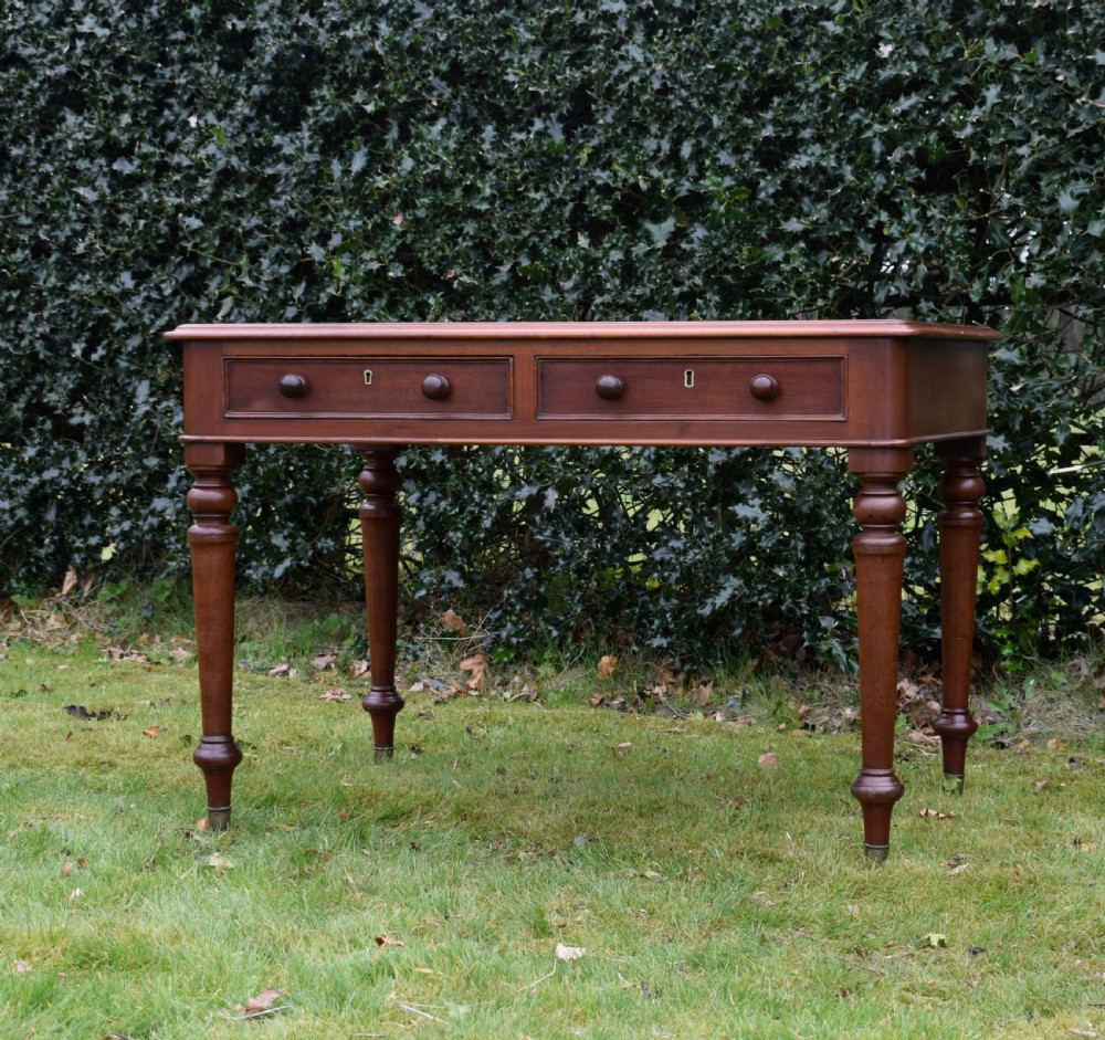 A Victorian mahogany writing table featuring a dark red leather insert top, two frieze drawers with wooden knobs, and four turned legs. View VII
