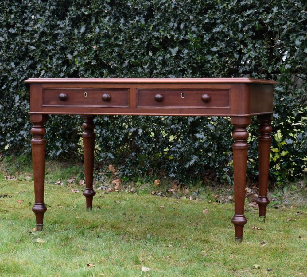 A Victorian mahogany writing table featuring a dark red leather insert top, two frieze drawers with wooden knobs, and four turned legs. View VIII