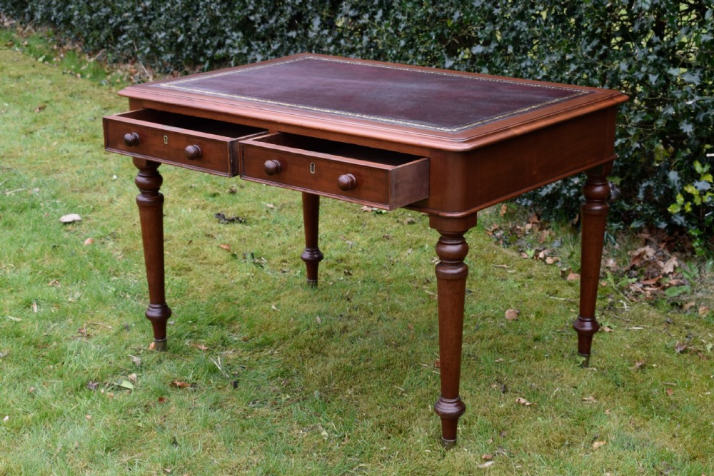 A Victorian mahogany writing table featuring a dark red leather insert top, two frieze drawers with wooden knobs, and four turned legs. View IX