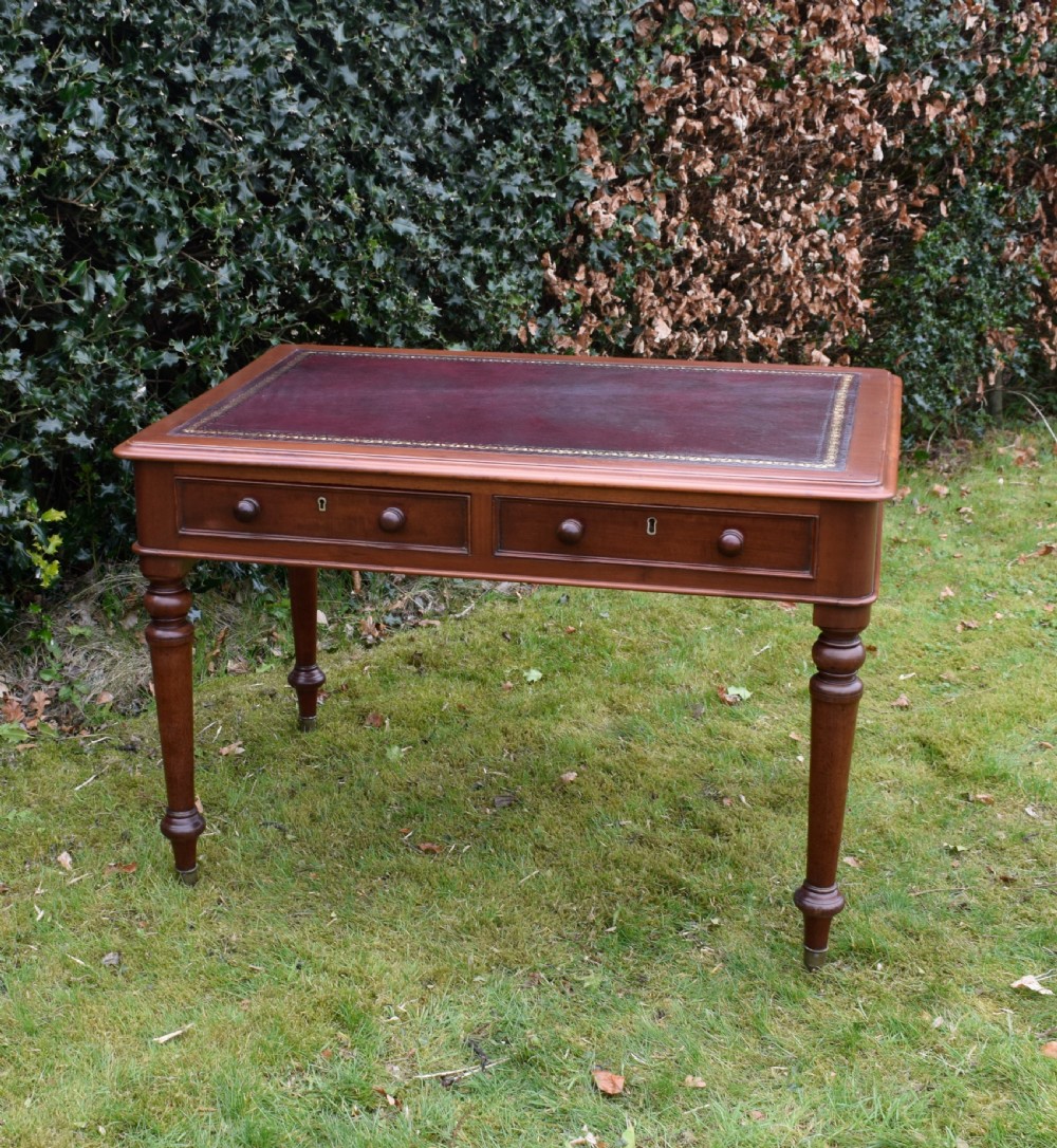 A Victorian mahogany writing table featuring a dark red leather insert top, two frieze drawers with wooden knobs, and four turned legs. View X