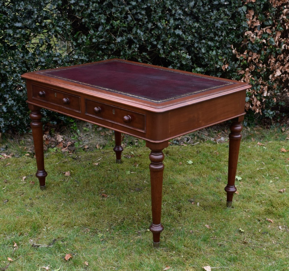 A Victorian mahogany writing table featuring a dark red leather insert top, two frieze drawers with wooden knobs, and four turned legs. View XI