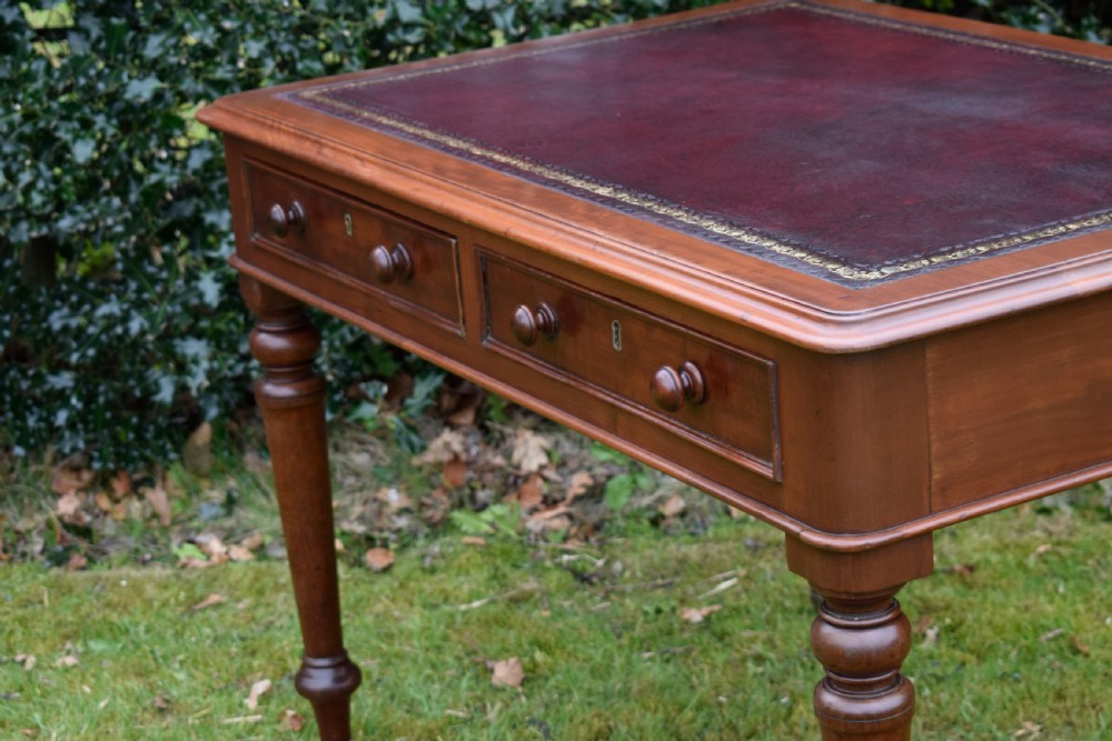 A Victorian mahogany writing table featuring a dark red leather insert top, two frieze drawers with wooden knobs, and four turned legs. View XII