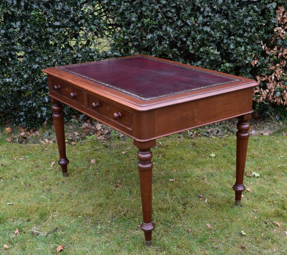 A Victorian mahogany writing table featuring a dark red leather insert top, two frieze drawers with wooden knobs, and four turned legs. View XIII