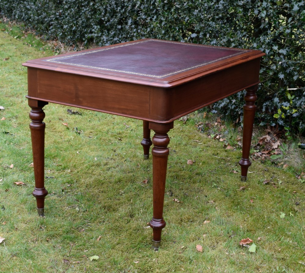 A Victorian mahogany writing table featuring a dark red leather insert top, two frieze drawers with wooden knobs, and four turned legs. View XV