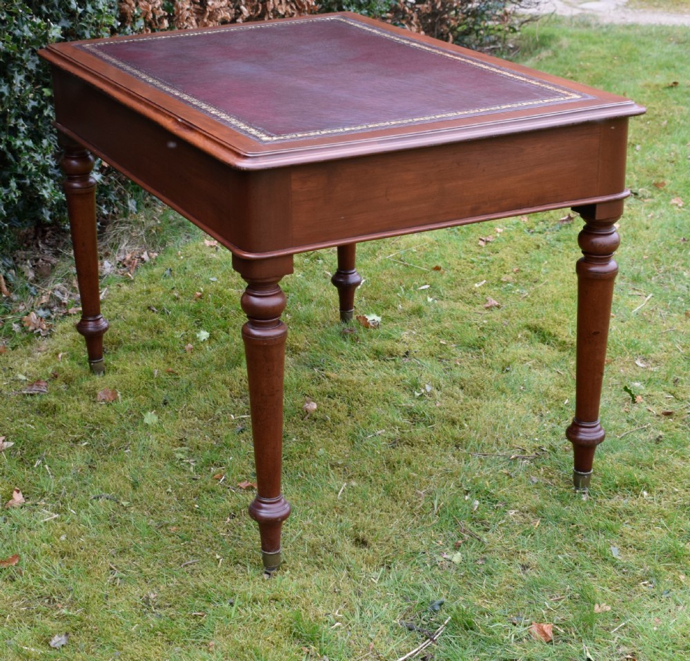 A Victorian mahogany writing table featuring a dark red leather insert top, two frieze drawers with wooden knobs, and four turned legs. View XVI