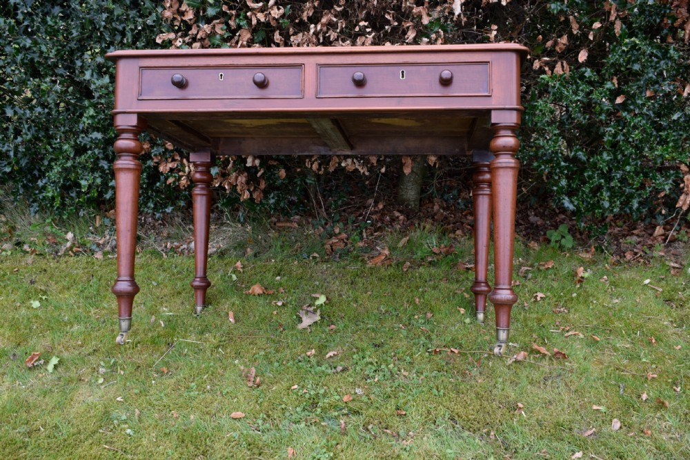 A Victorian mahogany writing table featuring a dark red leather insert top, two frieze drawers with wooden knobs, and four turned legs. View XVII