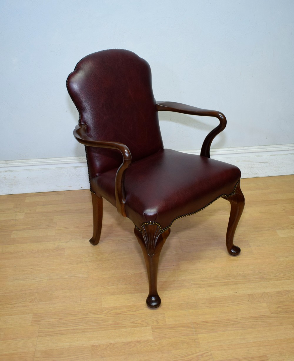 A dark burgundy leather upholstered library armchair featuring a carved walnut frame, open curved armrests, brass studding, and front cabriole legs.
