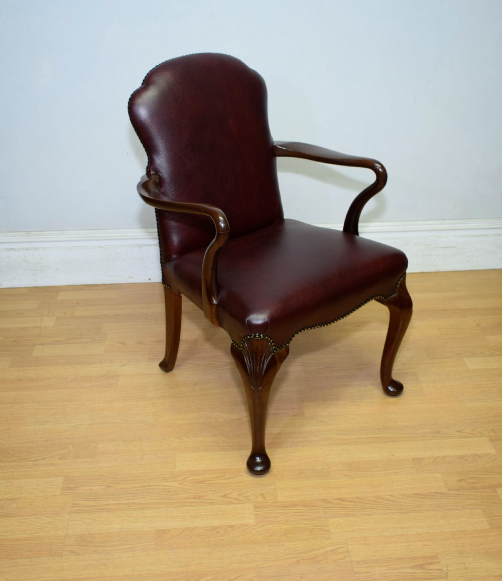A dark burgundy leather upholstered library armchair featuring a carved walnut frame, open curved armrests, brass studding, and front cabriole legs. View V