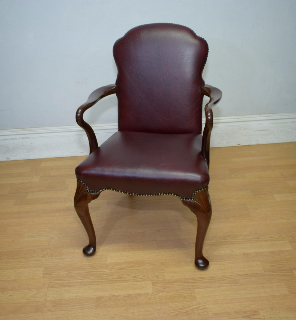 A dark burgundy leather upholstered library armchair featuring a carved walnut frame, open curved armrests, brass studding, and front cabriole legs. View VI