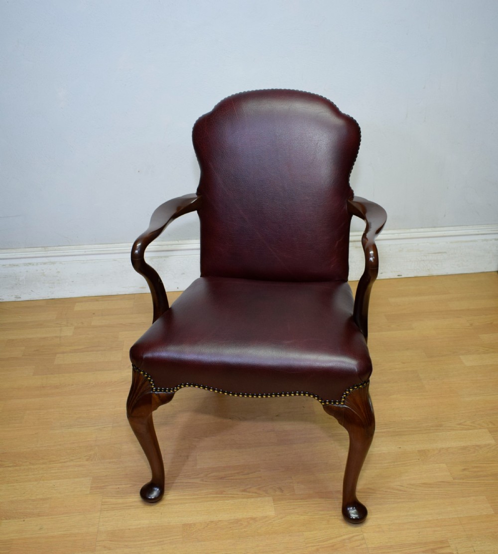 A dark burgundy leather upholstered library armchair featuring a carved walnut frame, open curved armrests, brass studding, and front cabriole legs. View VII