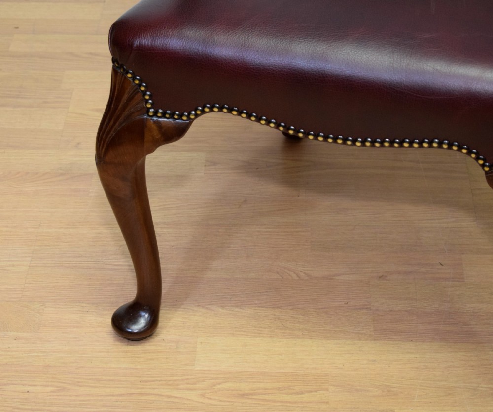 A dark burgundy leather upholstered library armchair featuring a carved walnut frame, open curved armrests, brass studding, and front cabriole legs. View IX