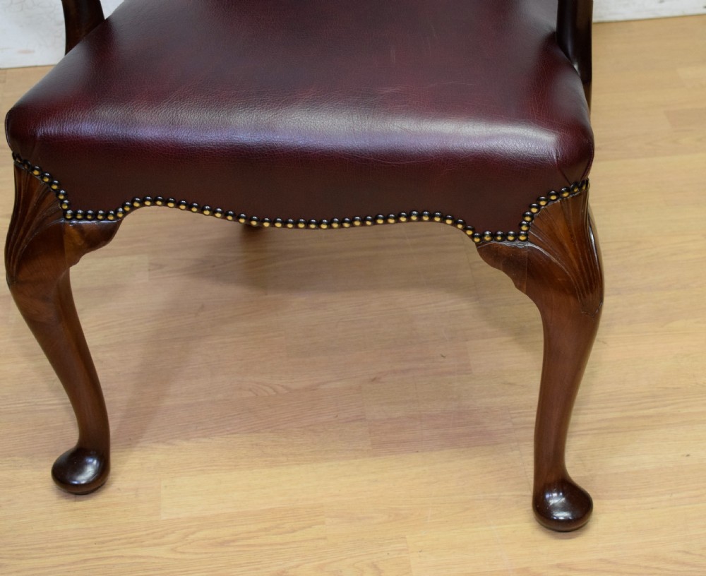 A dark burgundy leather upholstered library armchair featuring a carved walnut frame, open curved armrests, brass studding, and front cabriole legs. View X