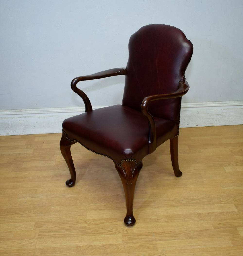 A dark burgundy leather upholstered library armchair featuring a carved walnut frame, open curved armrests, brass studding, and front cabriole legs. View XI