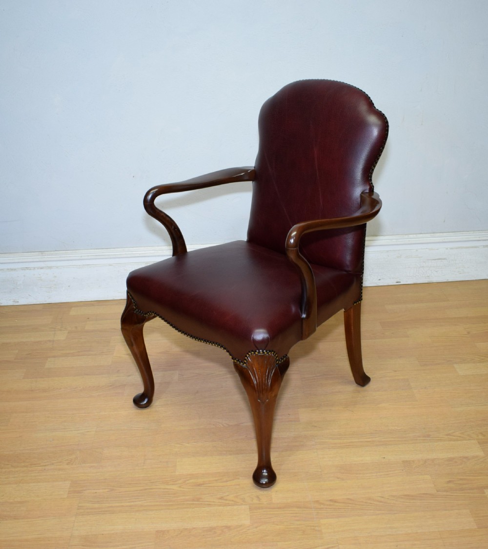 A dark burgundy leather upholstered library armchair featuring a carved walnut frame, open curved armrests, brass studding, and front cabriole legs. View XII