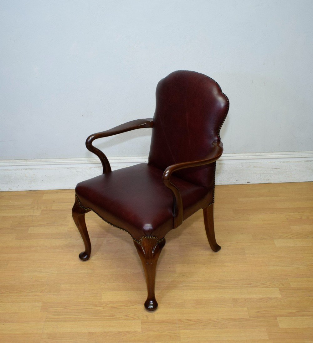 A dark burgundy leather upholstered library armchair featuring a carved walnut frame, open curved armrests, brass studding, and front cabriole legs. View XIII