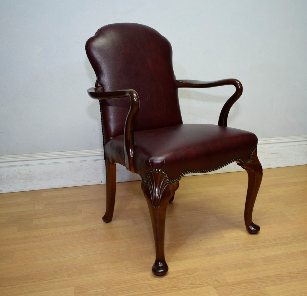 A dark burgundy leather upholstered library armchair featuring a carved walnut frame, open curved armrests, brass studding, and front cabriole legs. View XVI