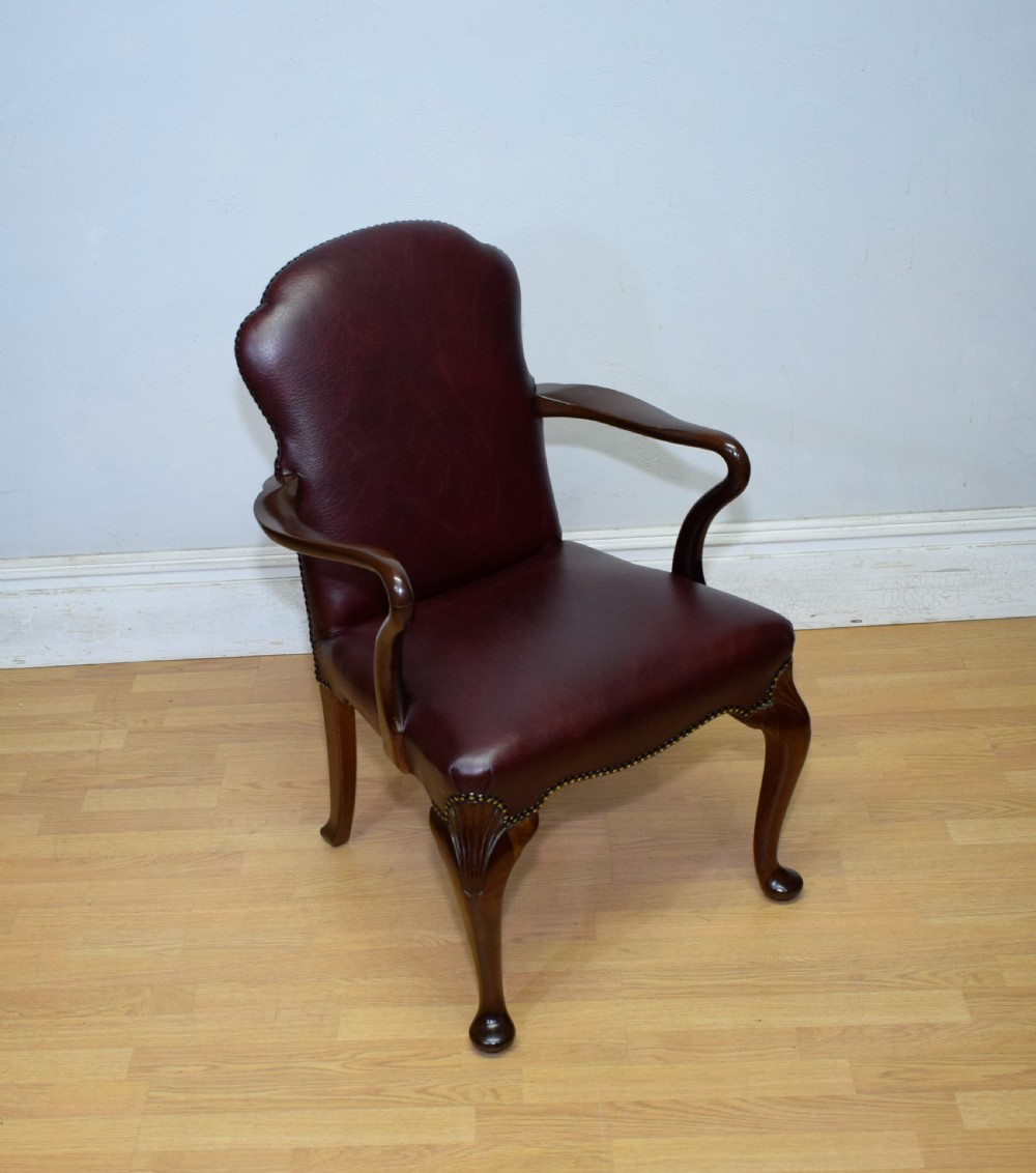 A dark burgundy leather upholstered library armchair featuring a carved walnut frame, open curved armrests, brass studding, and front cabriole legs. View XVII
