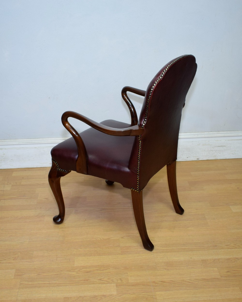 A dark burgundy leather upholstered library armchair featuring a carved walnut frame, open curved armrests, brass studding, and front cabriole legs. View XVIII