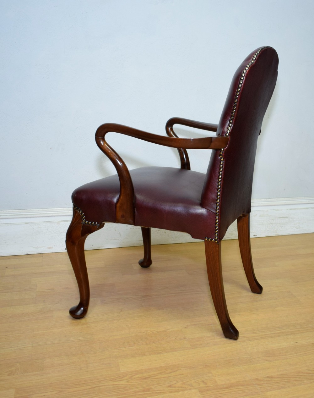 A dark burgundy leather upholstered library armchair featuring a carved walnut frame, open curved armrests, brass studding, and front cabriole legs. View XIX
