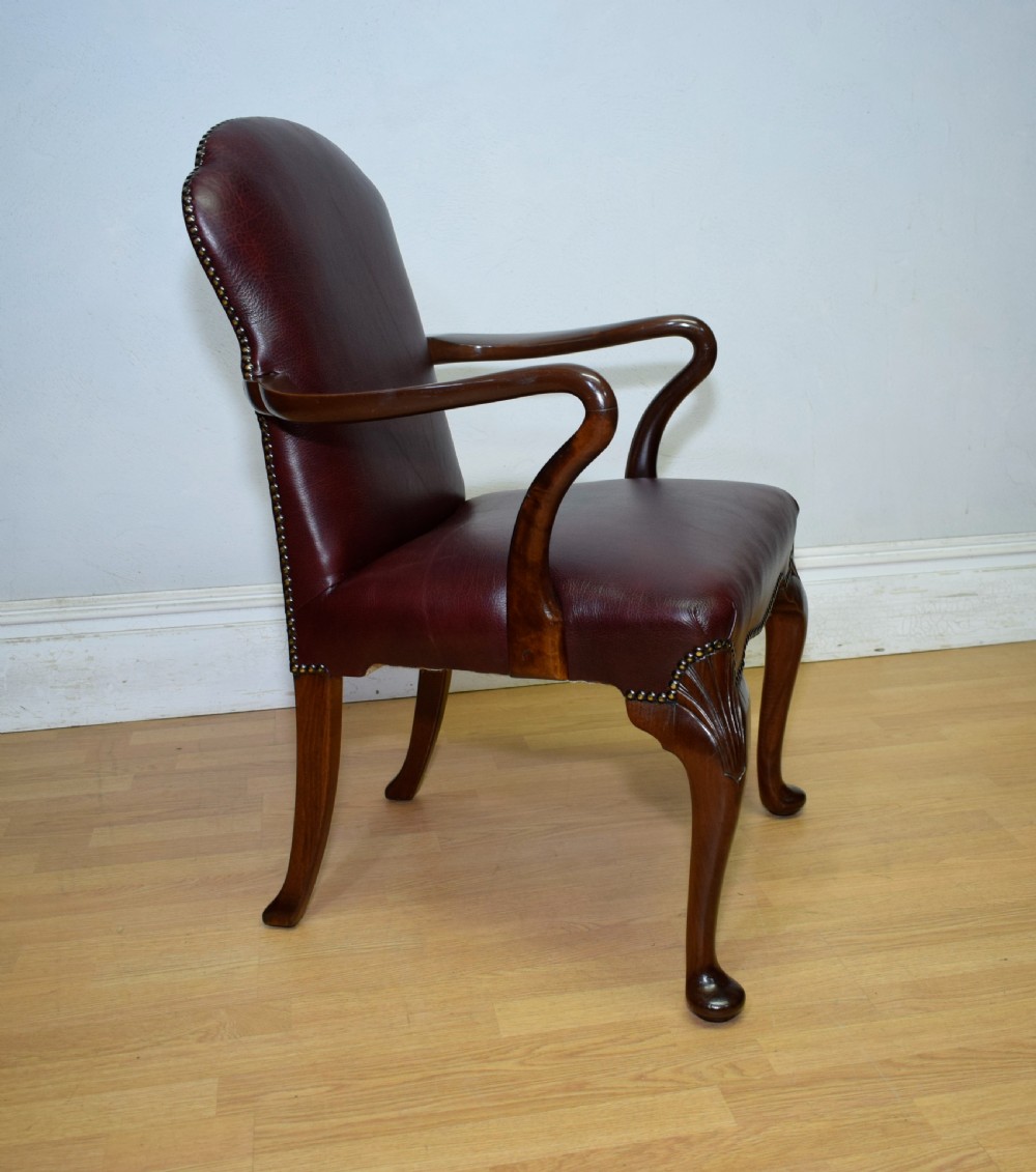 A dark burgundy leather upholstered library armchair featuring a carved walnut frame, open curved armrests, brass studding, and front cabriole legs. View XX