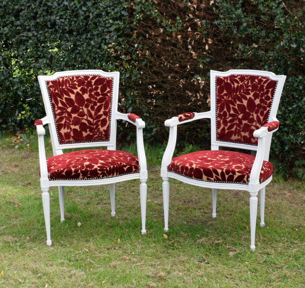 A pair of white painted open armchairs featuring fluted legs, padded armrests, and burgundy botanical cut velvet upholstery secured with brass studs. View II