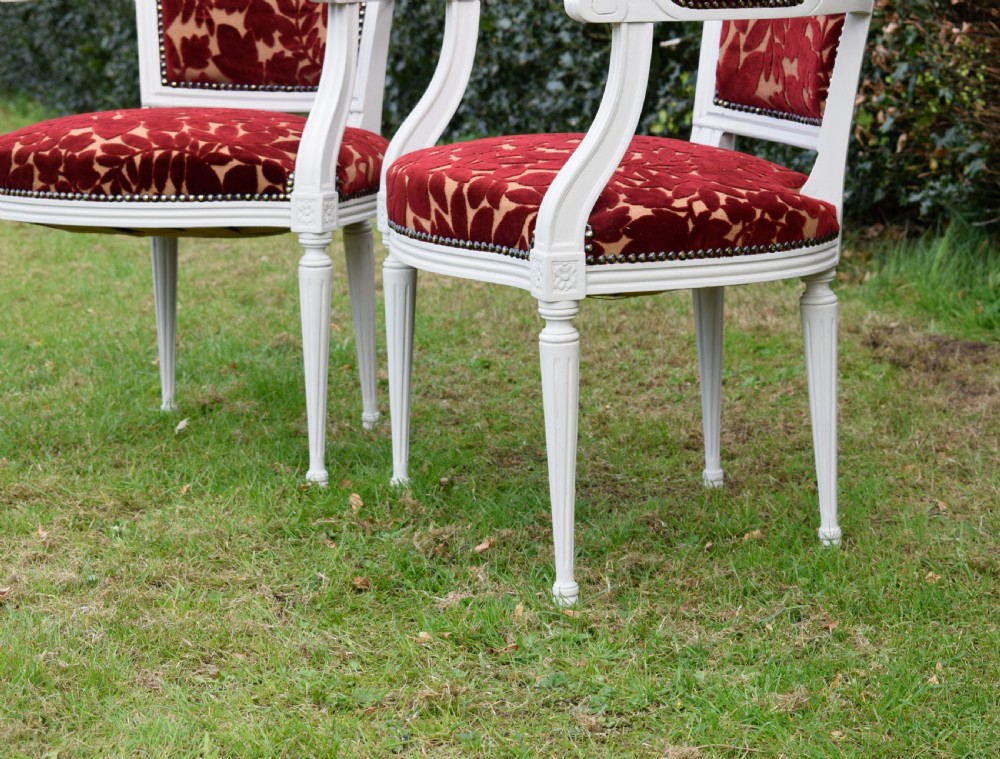 A pair of white painted open armchairs featuring fluted legs, padded armrests, and burgundy botanical cut velvet upholstery secured with brass studs. View V