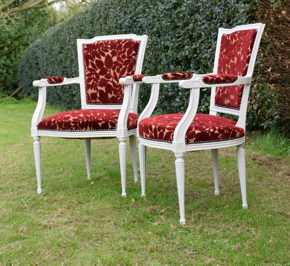 A pair of white painted open armchairs featuring fluted legs, padded armrests, and burgundy botanical cut velvet upholstery secured with brass studs. View VI