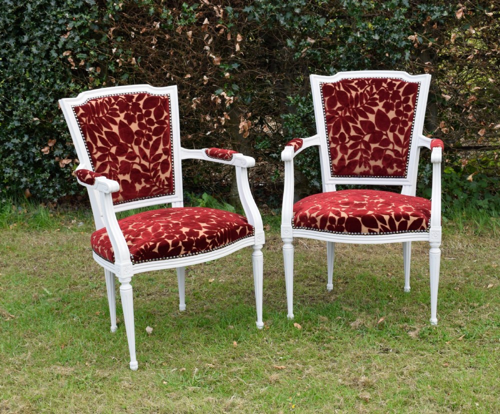 A pair of white painted open armchairs featuring fluted legs, padded armrests, and burgundy botanical cut velvet upholstery secured with brass studs. View VII