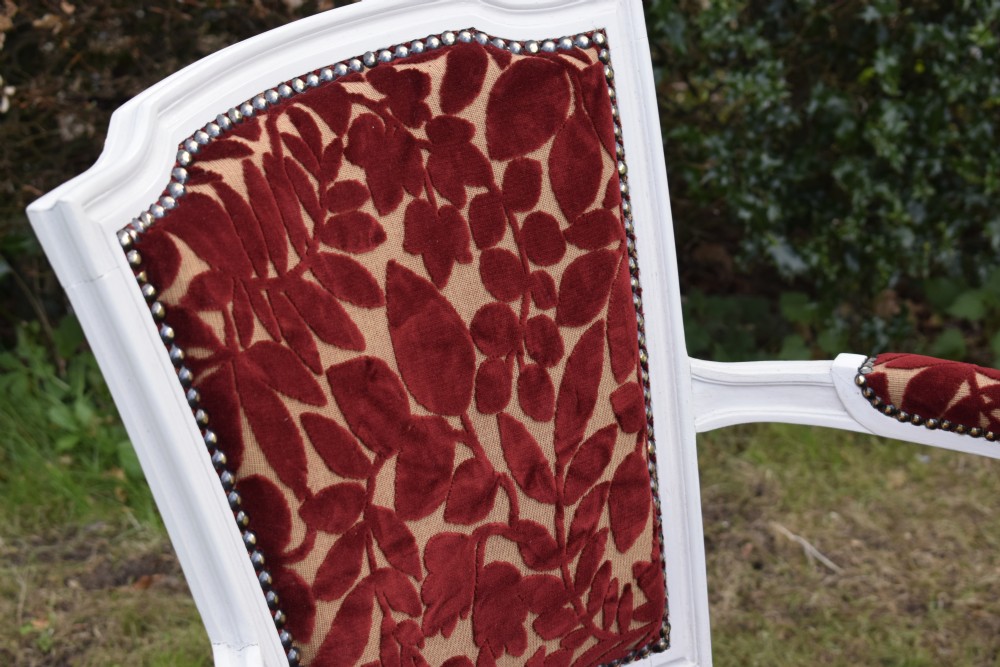 A pair of white painted open armchairs featuring fluted legs, padded armrests, and burgundy botanical cut velvet upholstery secured with brass studs. View IX