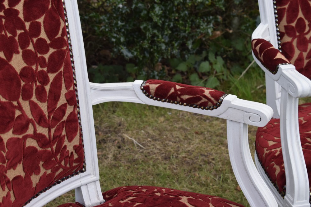 A pair of white painted open armchairs featuring fluted legs, padded armrests, and burgundy botanical cut velvet upholstery secured with brass studs. View XI