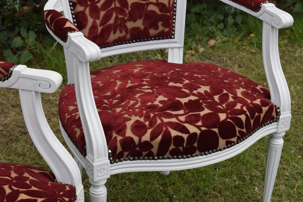 A pair of white painted open armchairs featuring fluted legs, padded armrests, and burgundy botanical cut velvet upholstery secured with brass studs. View XII