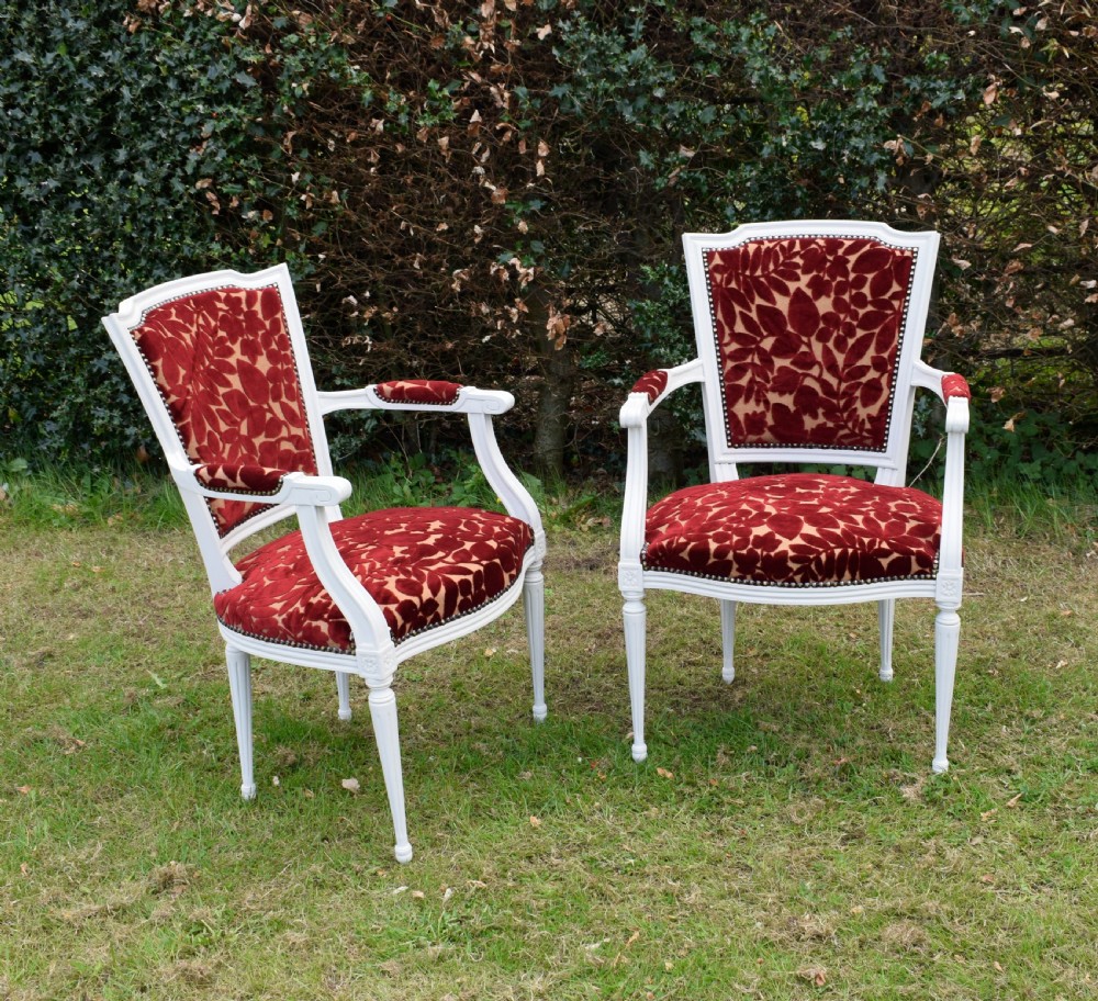A pair of white painted open armchairs featuring fluted legs, padded armrests, and burgundy botanical cut velvet upholstery secured with brass studs. View XIII