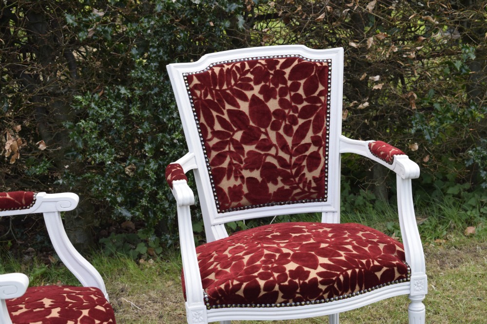 A pair of white painted open armchairs featuring fluted legs, padded armrests, and burgundy botanical cut velvet upholstery secured with brass studs. View XIV