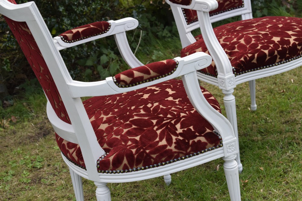 A pair of white painted open armchairs featuring fluted legs, padded armrests, and burgundy botanical cut velvet upholstery secured with brass studs. View XV