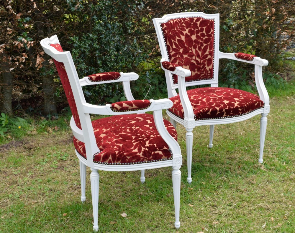 A pair of white painted open armchairs featuring fluted legs, padded armrests, and burgundy botanical cut velvet upholstery secured with brass studs. View XVI