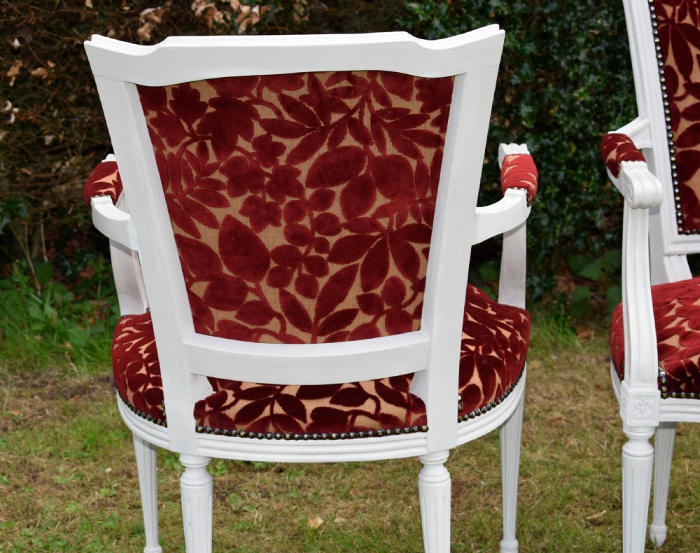 A pair of white painted open armchairs featuring fluted legs, padded armrests, and burgundy botanical cut velvet upholstery secured with brass studs. View XVIII