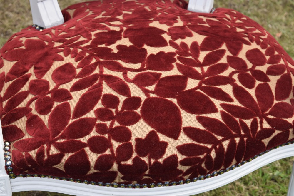 A pair of white painted open armchairs featuring fluted legs, padded armrests, and burgundy botanical cut velvet upholstery secured with brass studs. View XIX