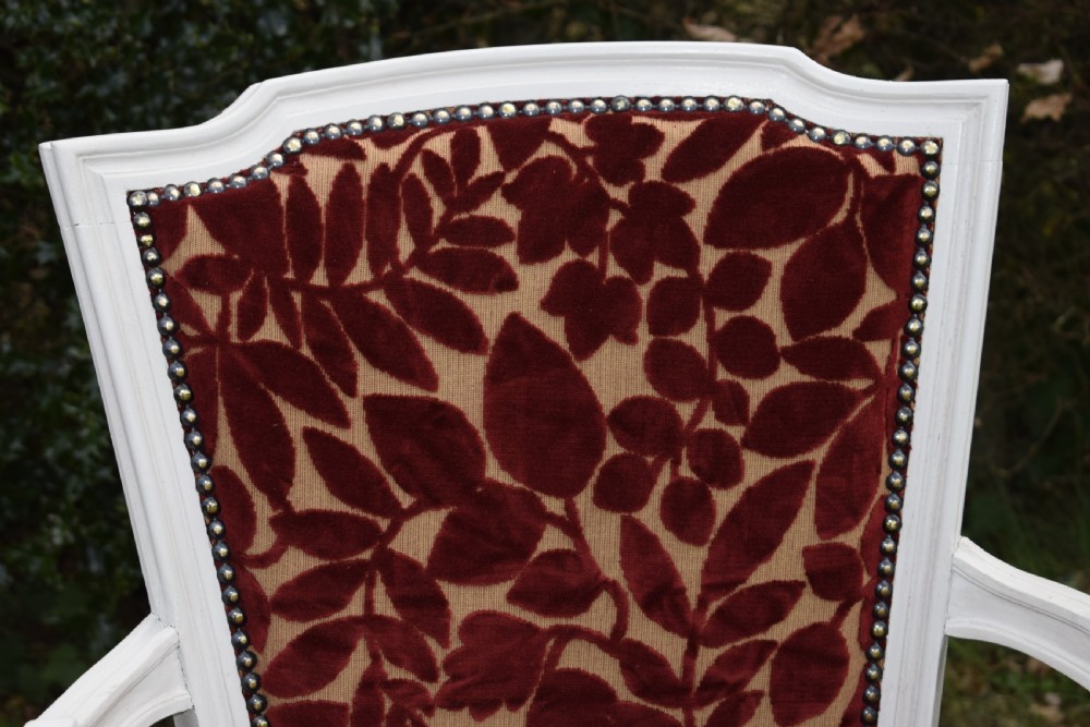 A pair of white painted open armchairs featuring fluted legs, padded armrests, and burgundy botanical cut velvet upholstery secured with brass studs. View XX