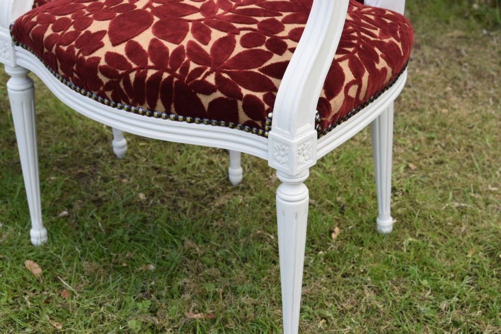 A pair of white painted open armchairs featuring fluted legs, padded armrests, and burgundy botanical cut velvet upholstery secured with brass studs. View XXI