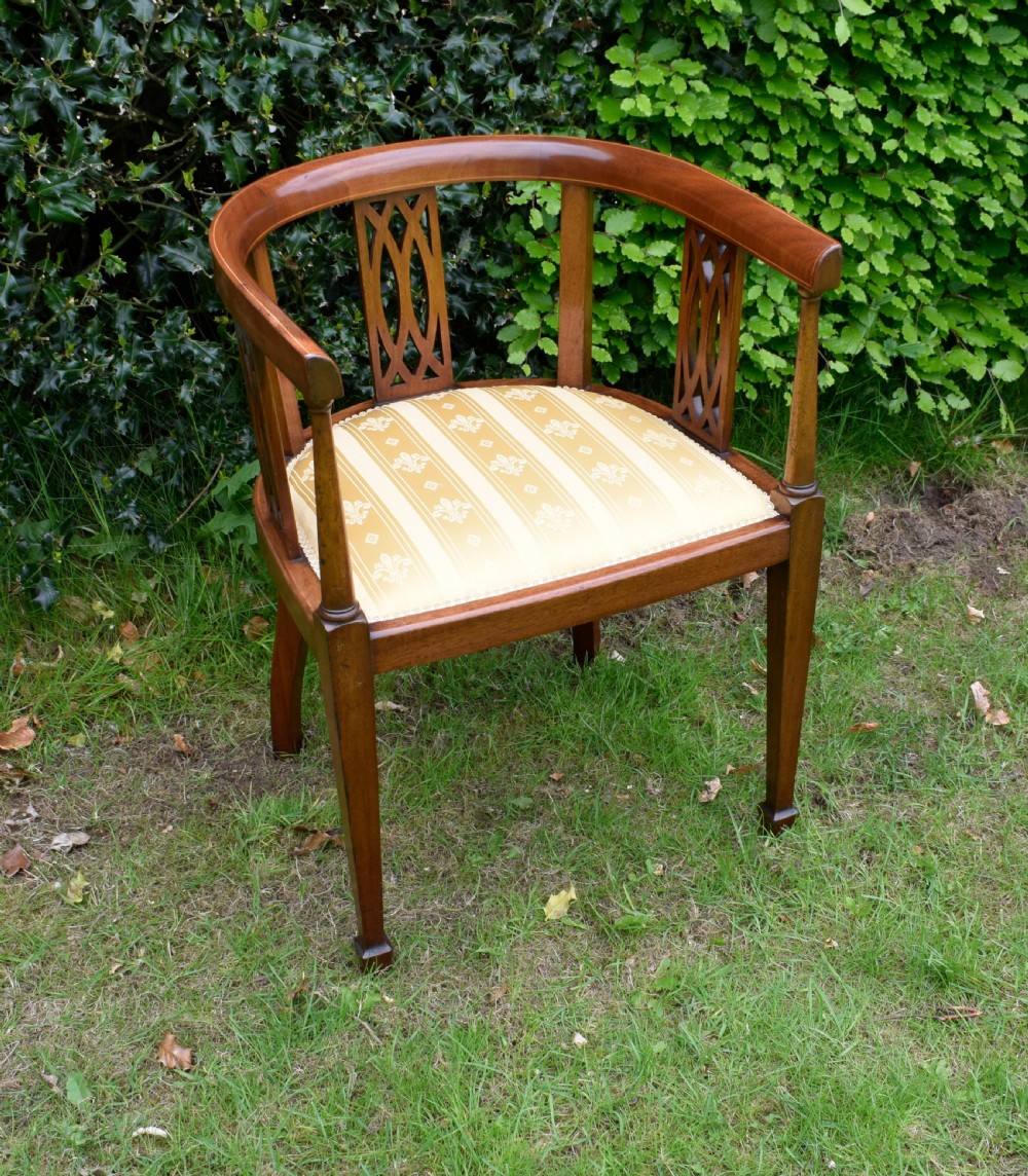 An Edwardian inlaid mahogany tub chair featuring a rounded crest rail, pierced geometric splats, and a gold striped upholstered seat.