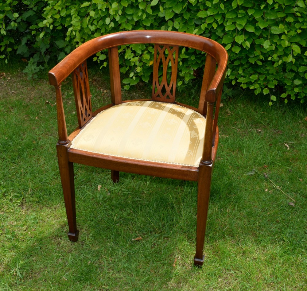 An Edwardian inlaid mahogany tub chair featuring a rounded crest rail, pierced geometric splats, and a gold striped upholstered seat. View II