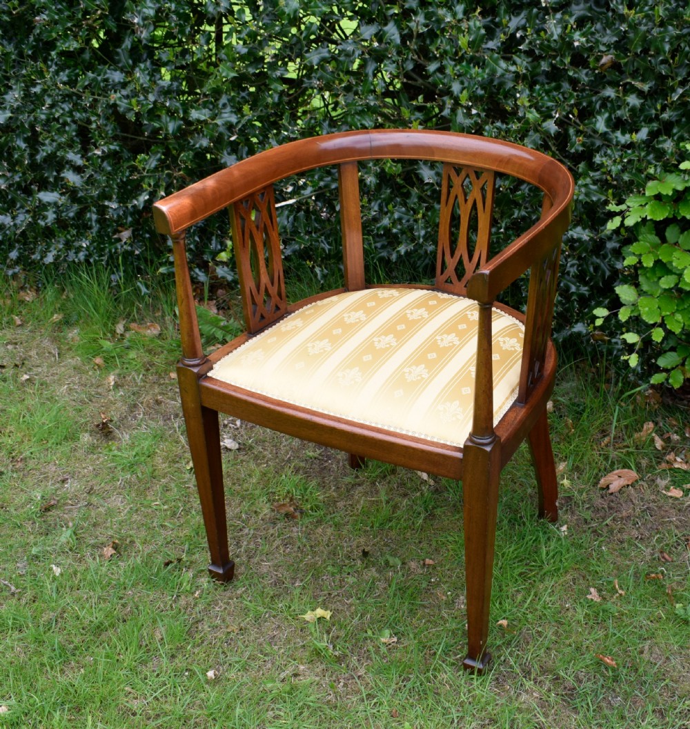 An Edwardian inlaid mahogany tub chair featuring a rounded crest rail, pierced geometric splats, and a gold striped upholstered seat. View IX