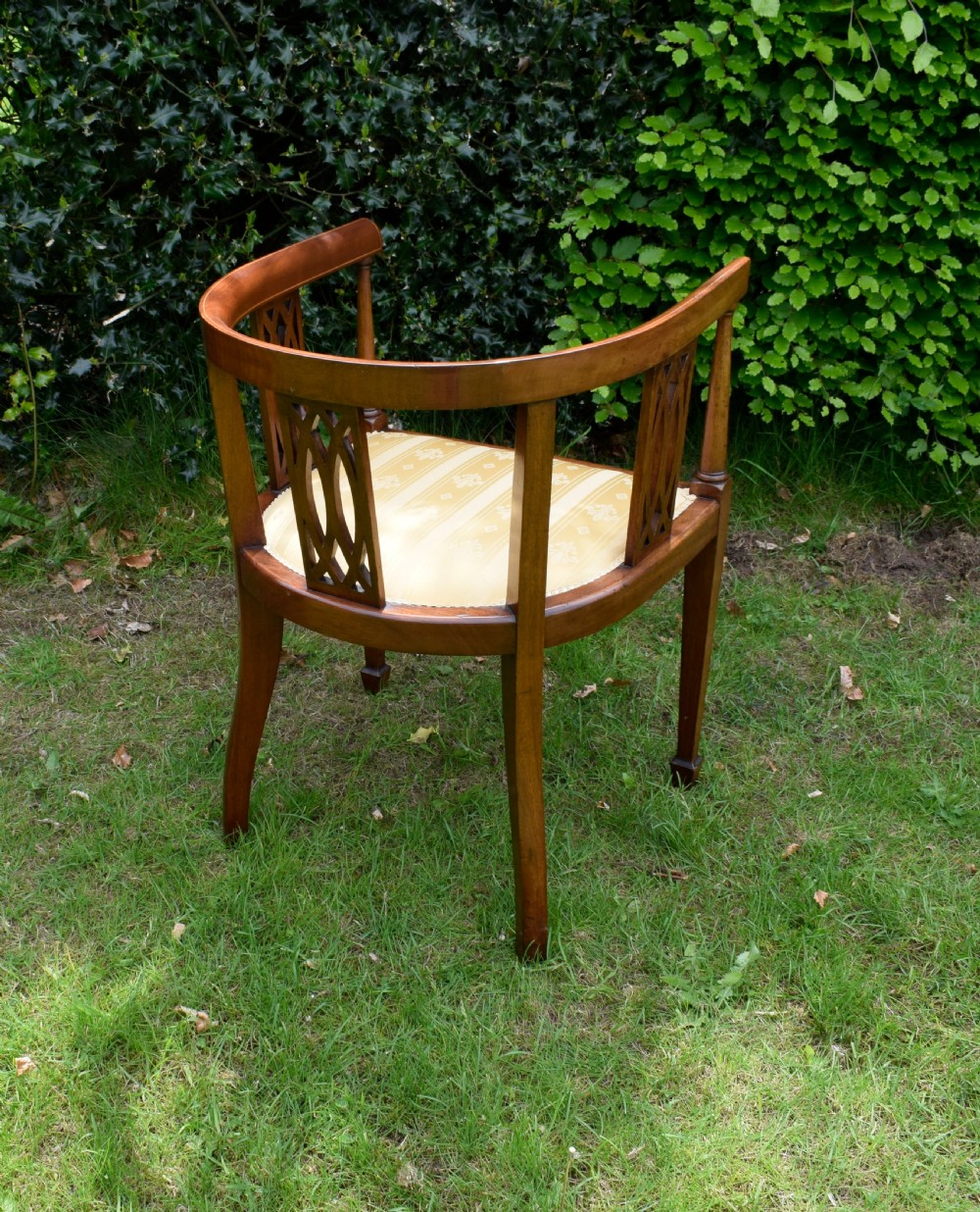 An Edwardian inlaid mahogany tub chair featuring a rounded crest rail, pierced geometric splats, and a gold striped upholstered seat. View XI