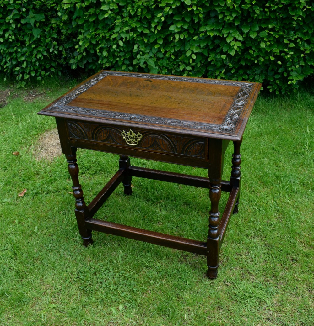A dark oak 17th-century lowboy table featuring a carved rectangular top, a single carved drawer front with a central brass handle, turned legs, and low wooden stretchers. View II