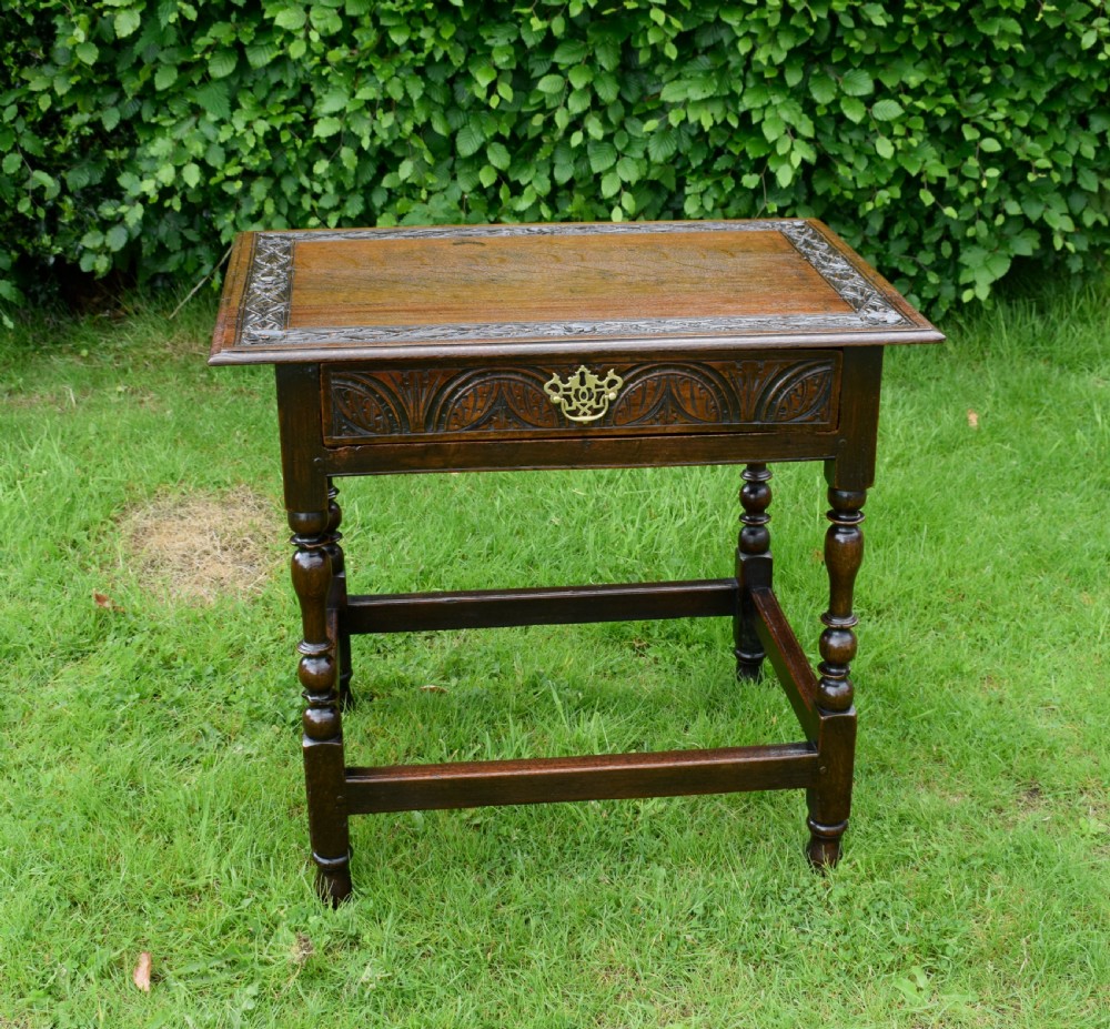 A dark oak 17th-century lowboy table featuring a carved rectangular top, a single carved drawer front with a central brass handle, turned legs, and low wooden stretchers. View IV