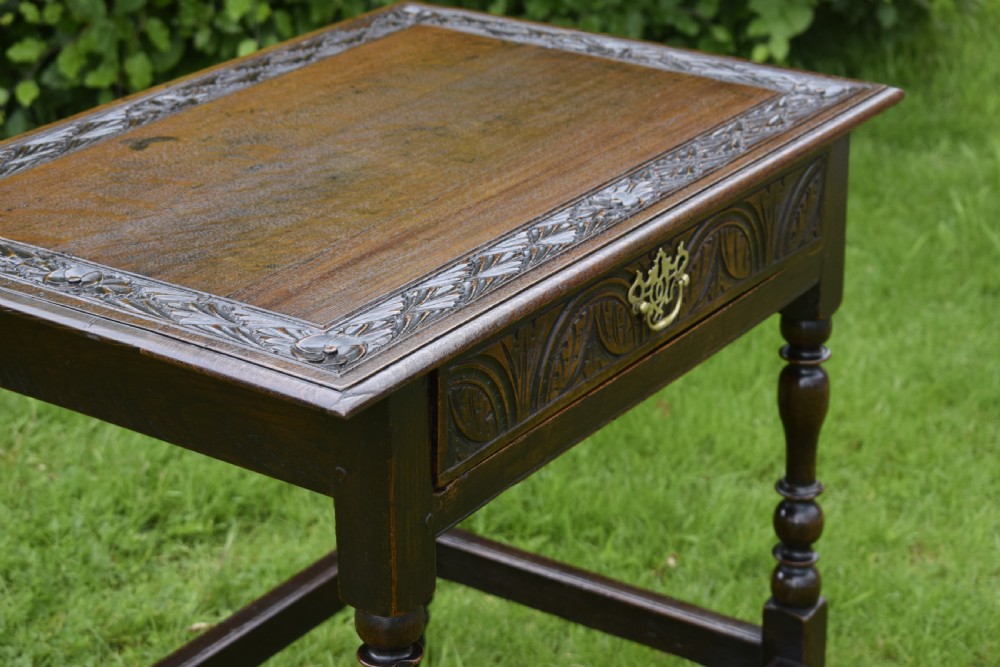 A dark oak 17th-century lowboy table featuring a carved rectangular top, a single carved drawer front with a central brass handle, turned legs, and low wooden stretchers. View VI